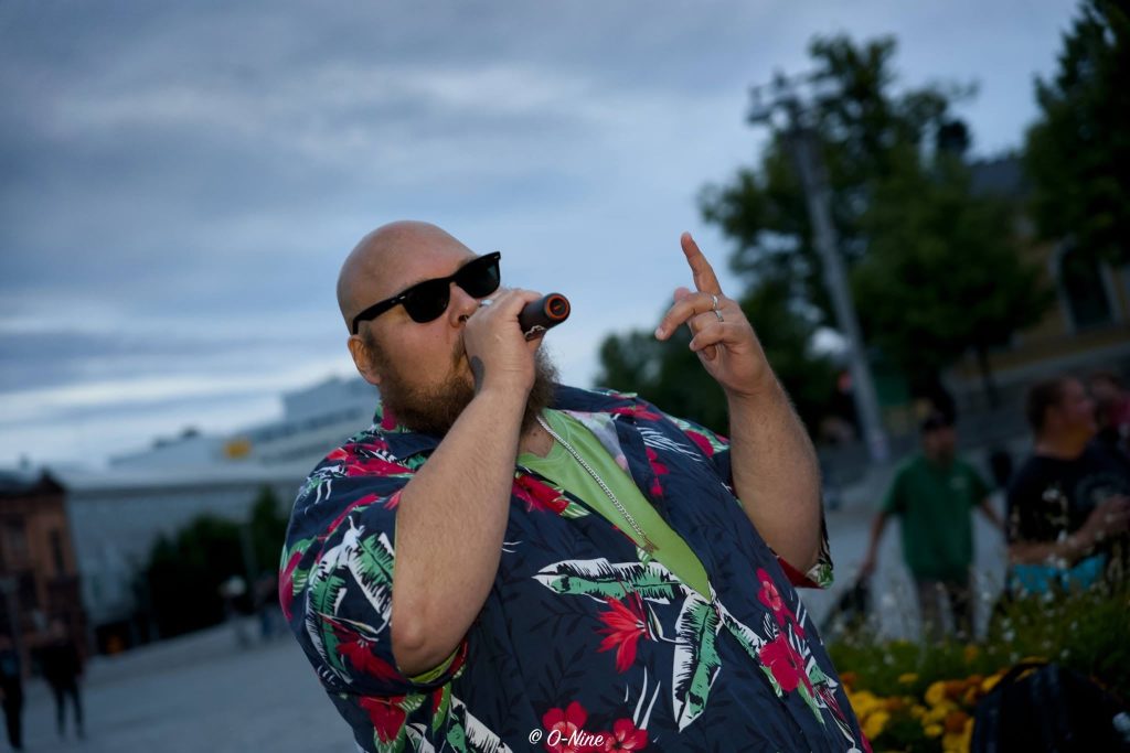 Läski Salonen räppää mikrofoniin aurinkolasit päässä ja kukkapaita yllä